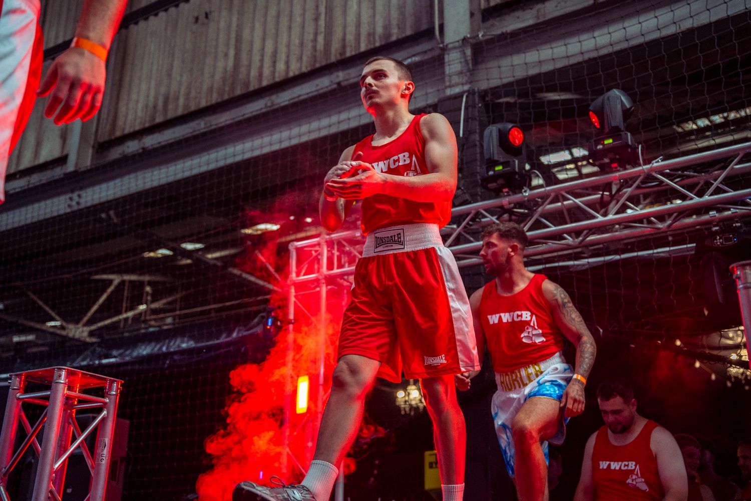 A boxer stands in a boxing ring illuminated by dramatic red lighting during a boxing match event.