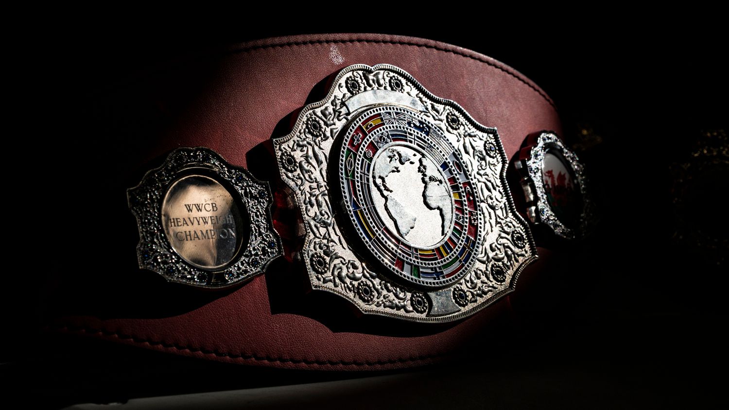Leather belt with silver circular metal and leather buckle displayed in detail against black background.