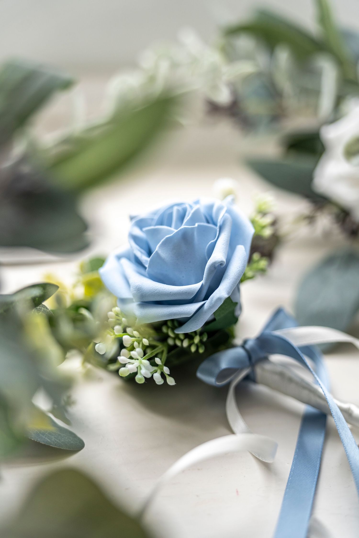 Light blue rose boutonniere with eucalyptus leaves and white ribbon detail.