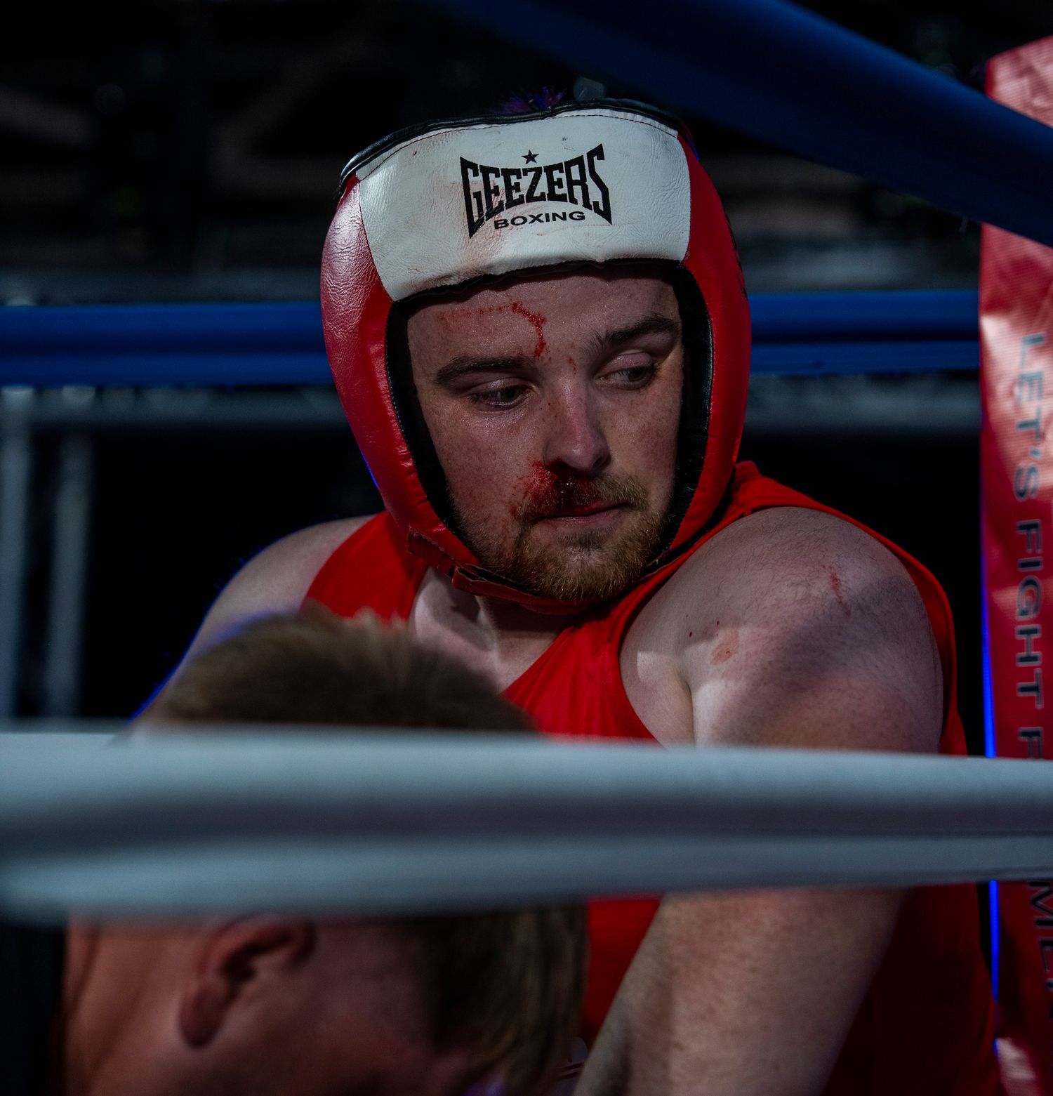 Amateur boxer wearing red protective headgear and Rezerz cap looks down during a match.