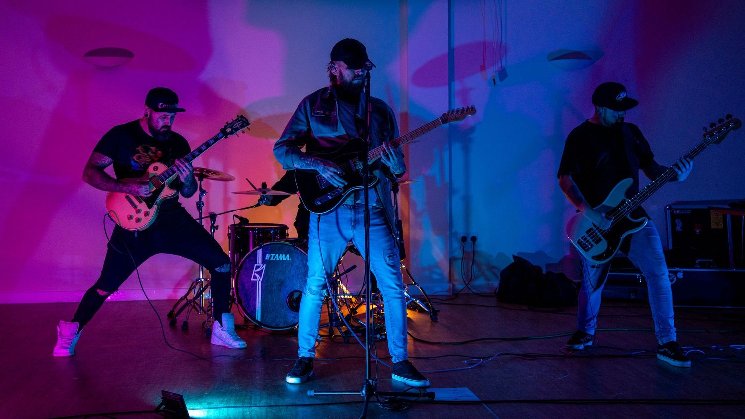 Rock band performing on stage with dramatic purple and blue lighting while musicians play guitars and drums.