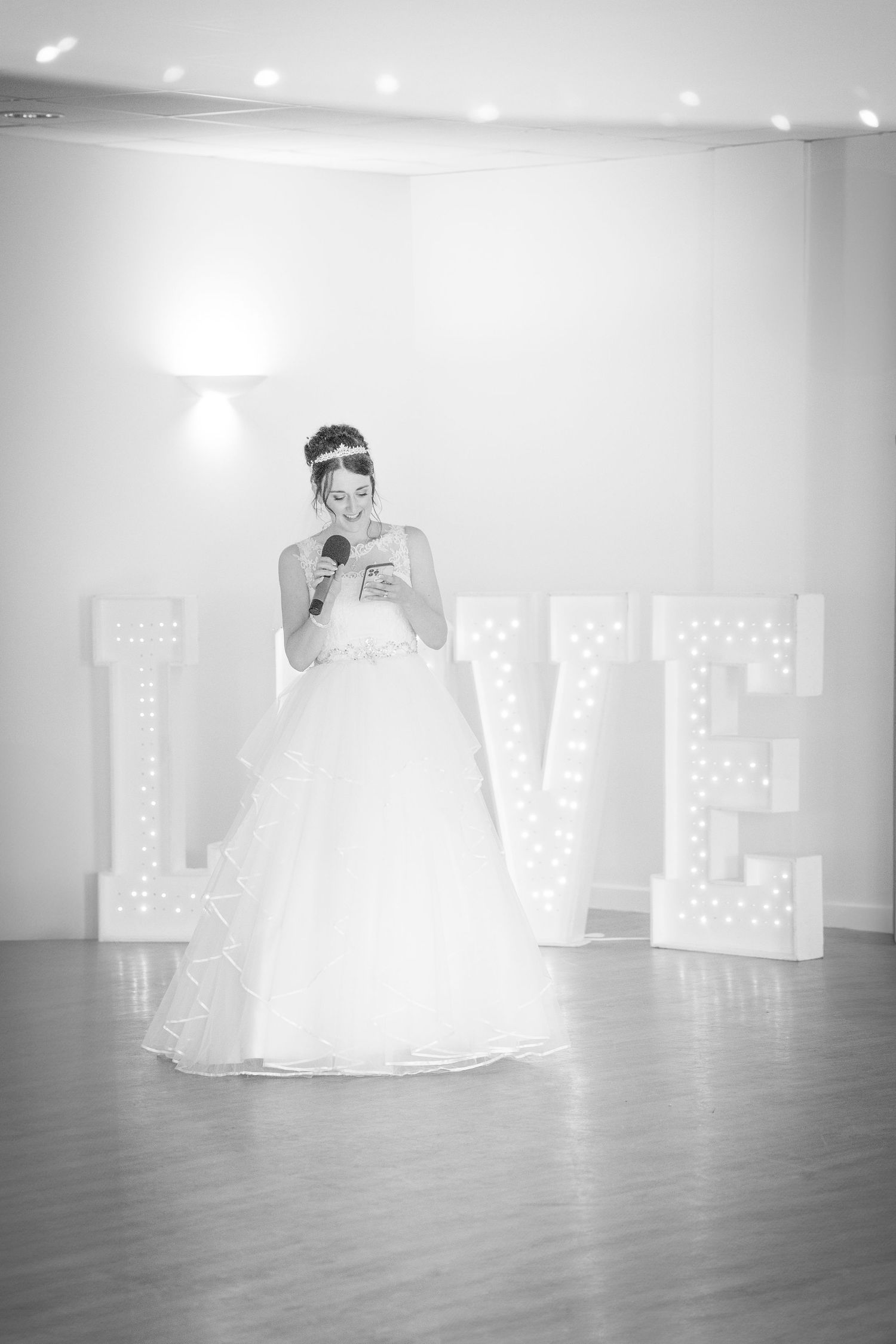 Five sequential black and white photos show decorative illuminated LOVE letters with a wedding dress in a reception venue.