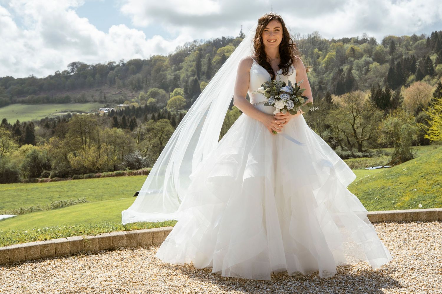 Wedding couple photographed against sweeping countryside views and dramatic cloudy sky.