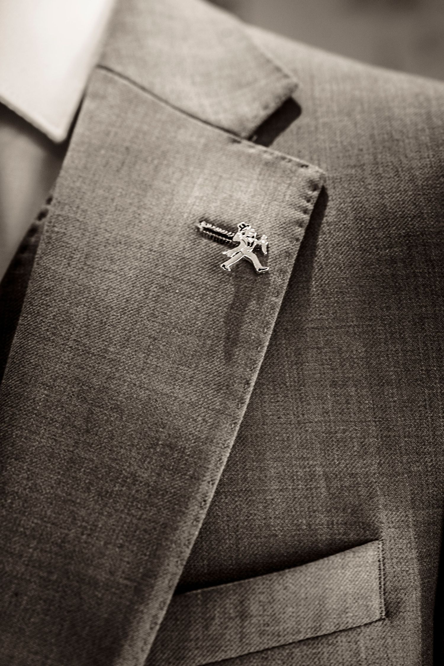 Close-up detail of a silver lapel pin on gray suit fabric.