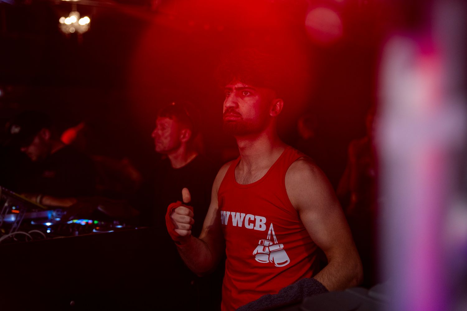 Multiple similar photos taken in a dark club or venue with red lighting show a figure in a sleeveless shirt performing on stage.
