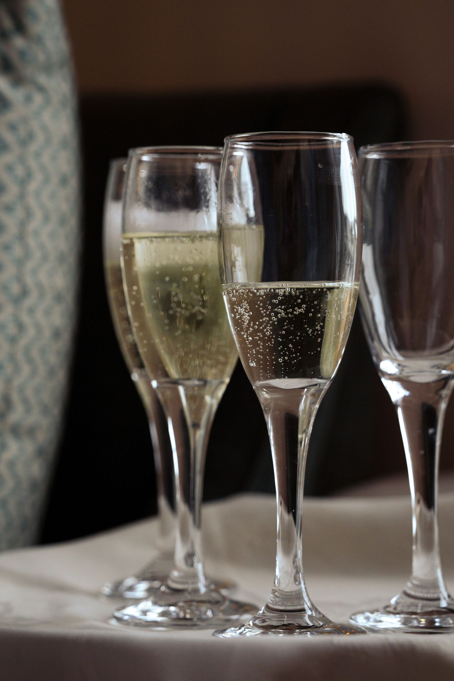 Clear champagne flutes lined up on a table with sparkling wine bubbles rising in the glasses.