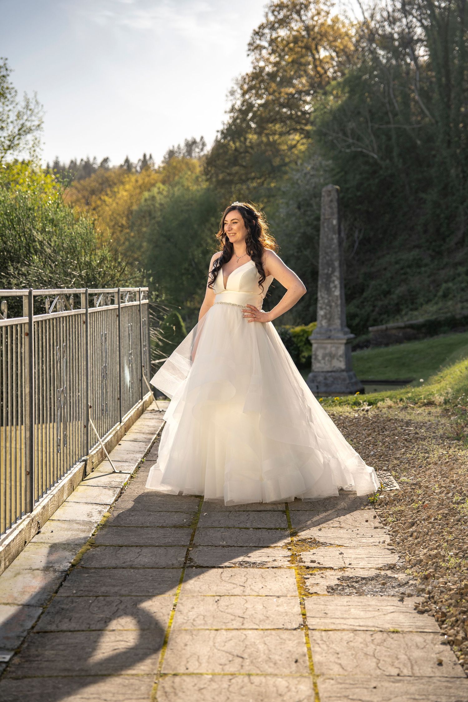 Beautiful wedding dress flowing in sunlight on stone pathway with metal railings.