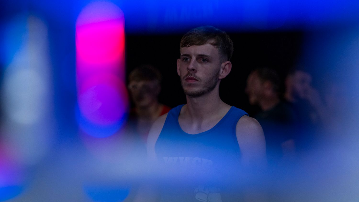 Professional boxer strikes a serious pose during a pre-fight event with blue and pink lighting effects.