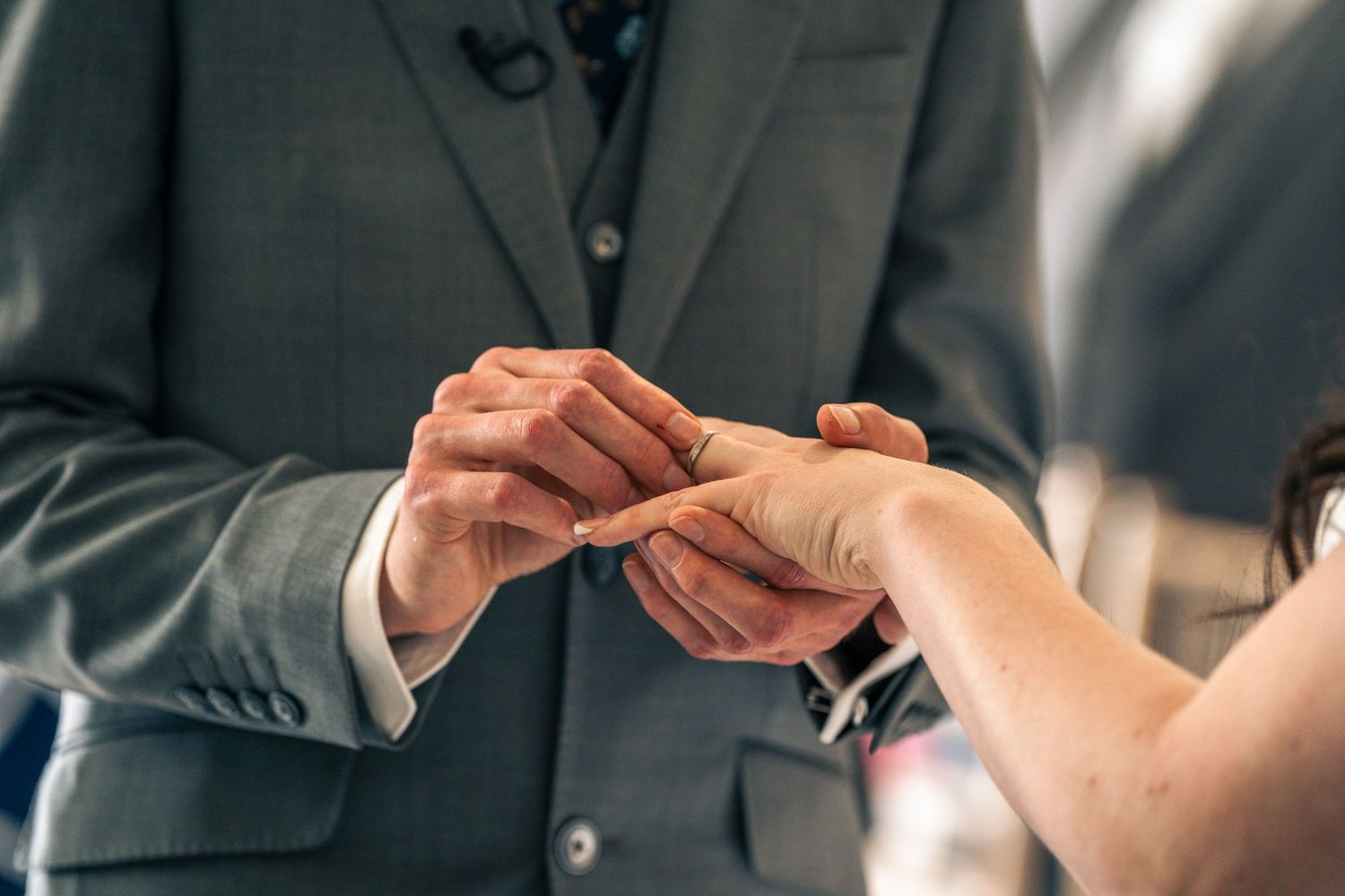 Close-up of hands exchanging wedding rings during ceremony.
