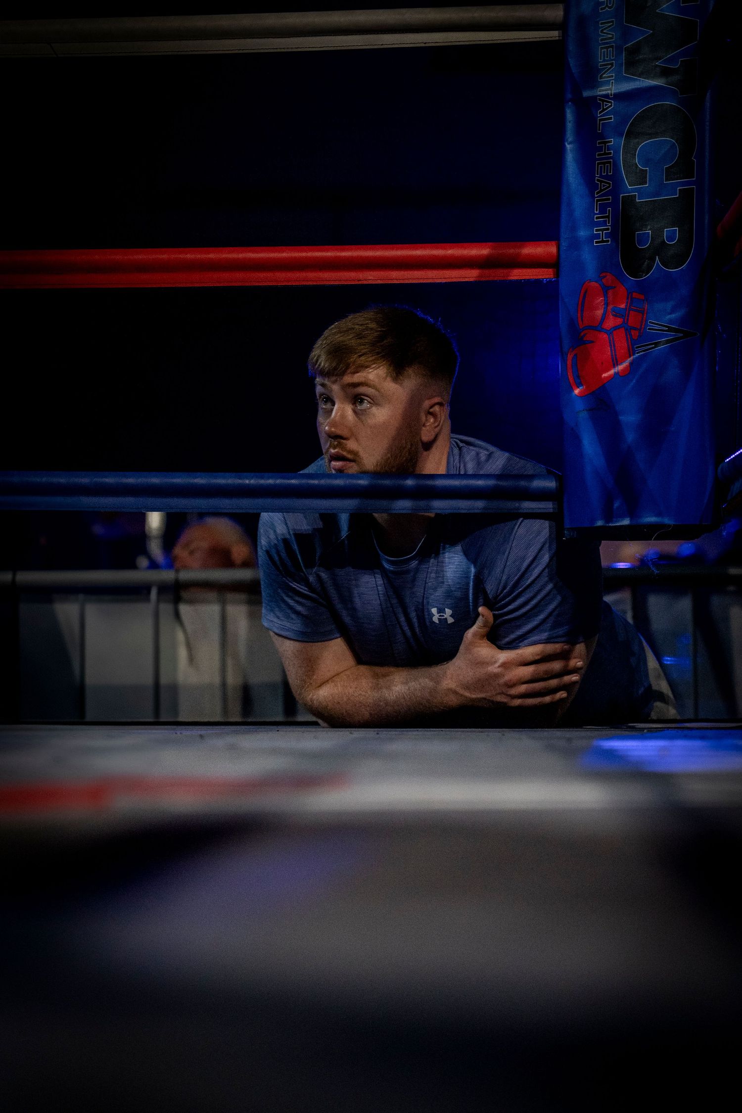 Person peering intensely through blue-lit window or opening with dramatic lighting and shadows.