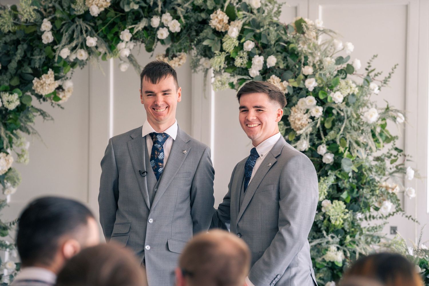 Wedding ceremony setup with floral arch and guests in formal attire.