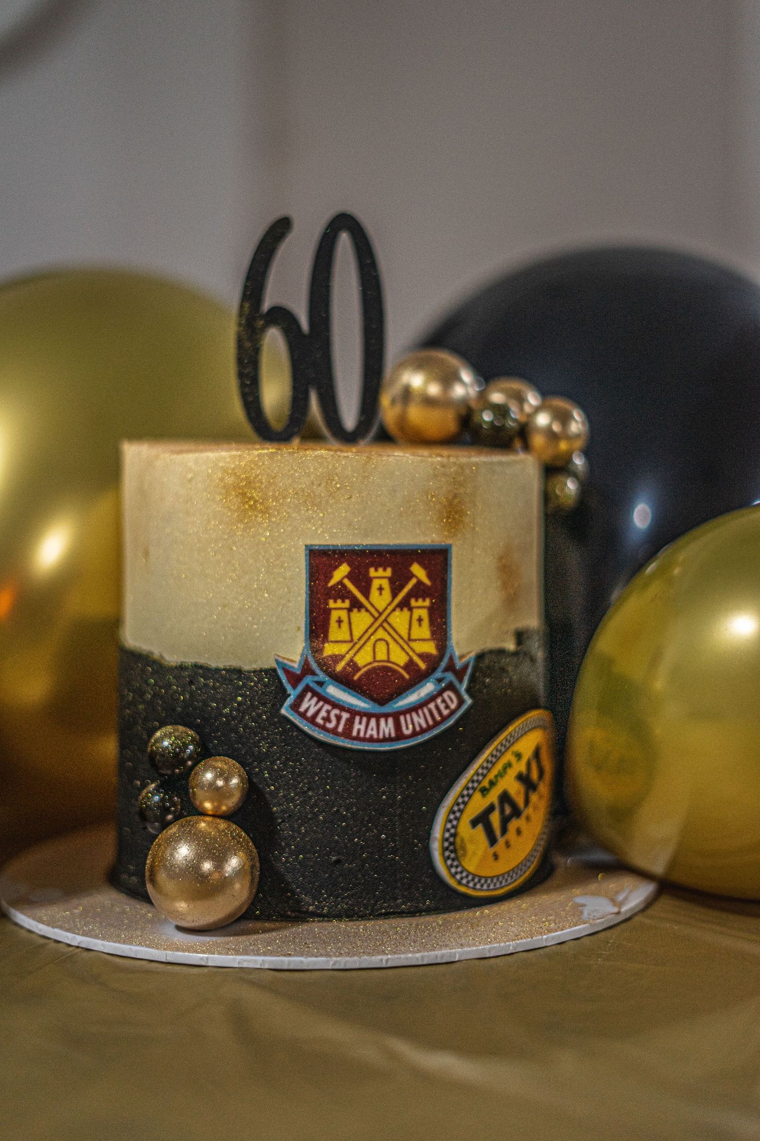 Close-up of modern West Ham United football badge embossed on black icing against gold and white cake decoration.