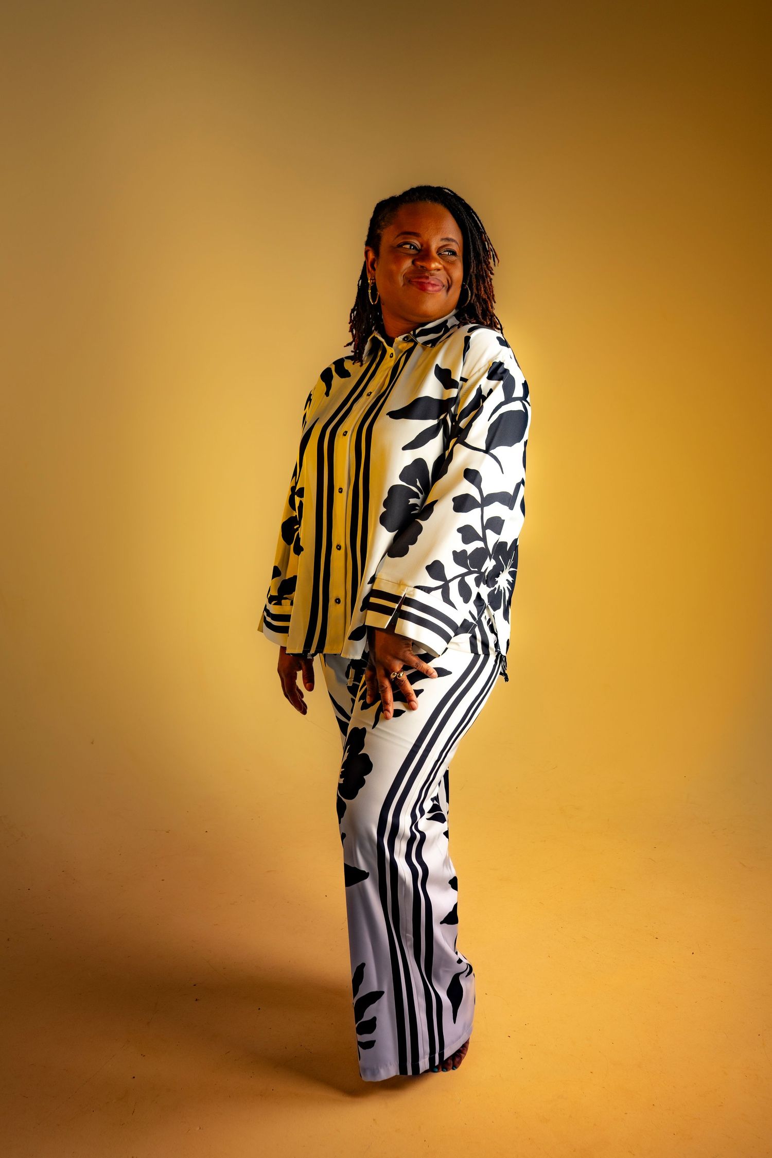 Fashion model poses in black and white graphic print dress against golden backdrop in studio photoshoot.