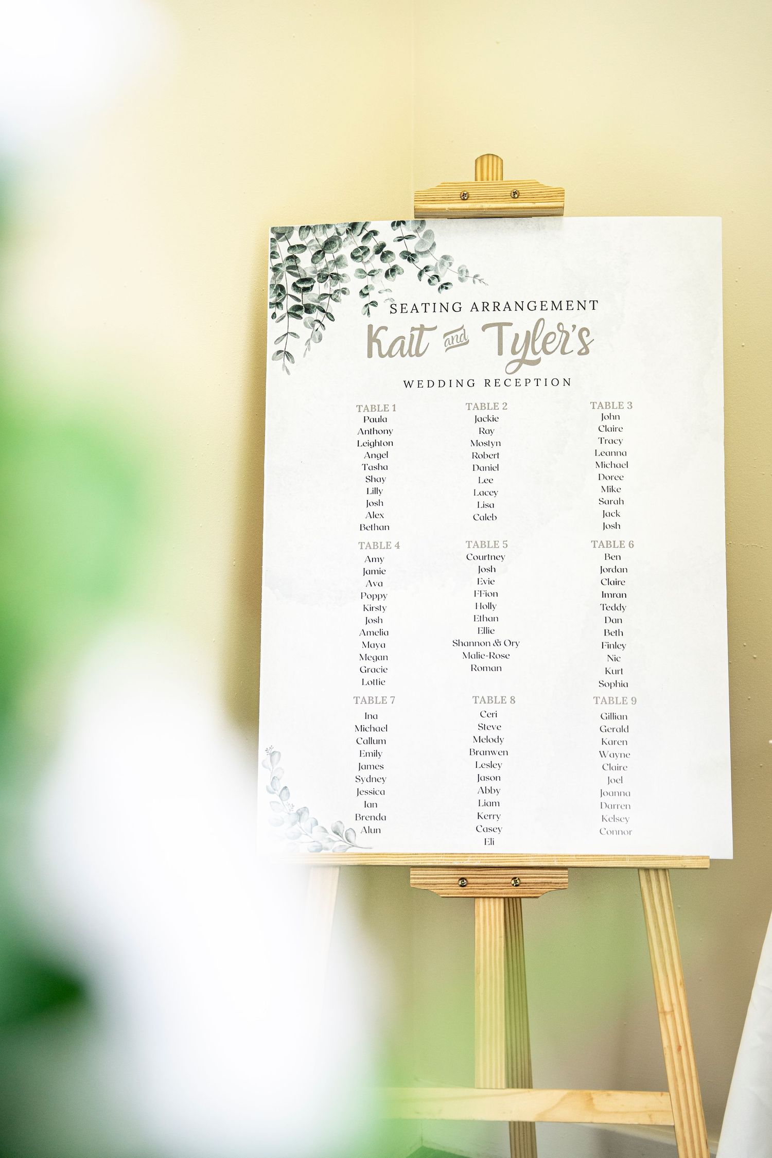 Wedding reception seating chart displayed on a wooden easel against a light beige background.