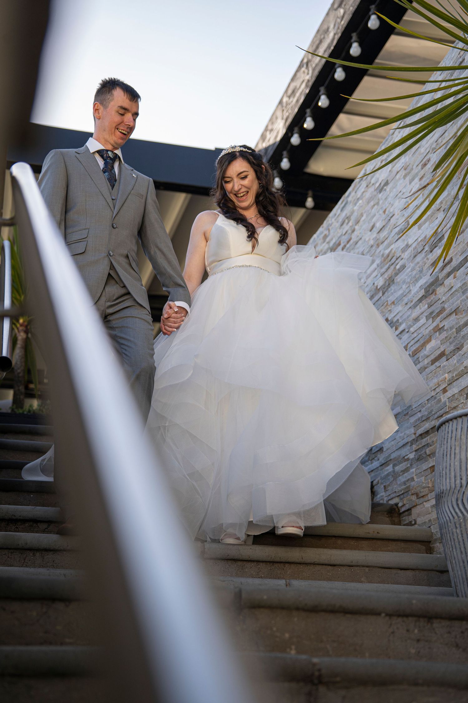 Couple descending stone stairs in formal wedding attire with dramatic lighting.