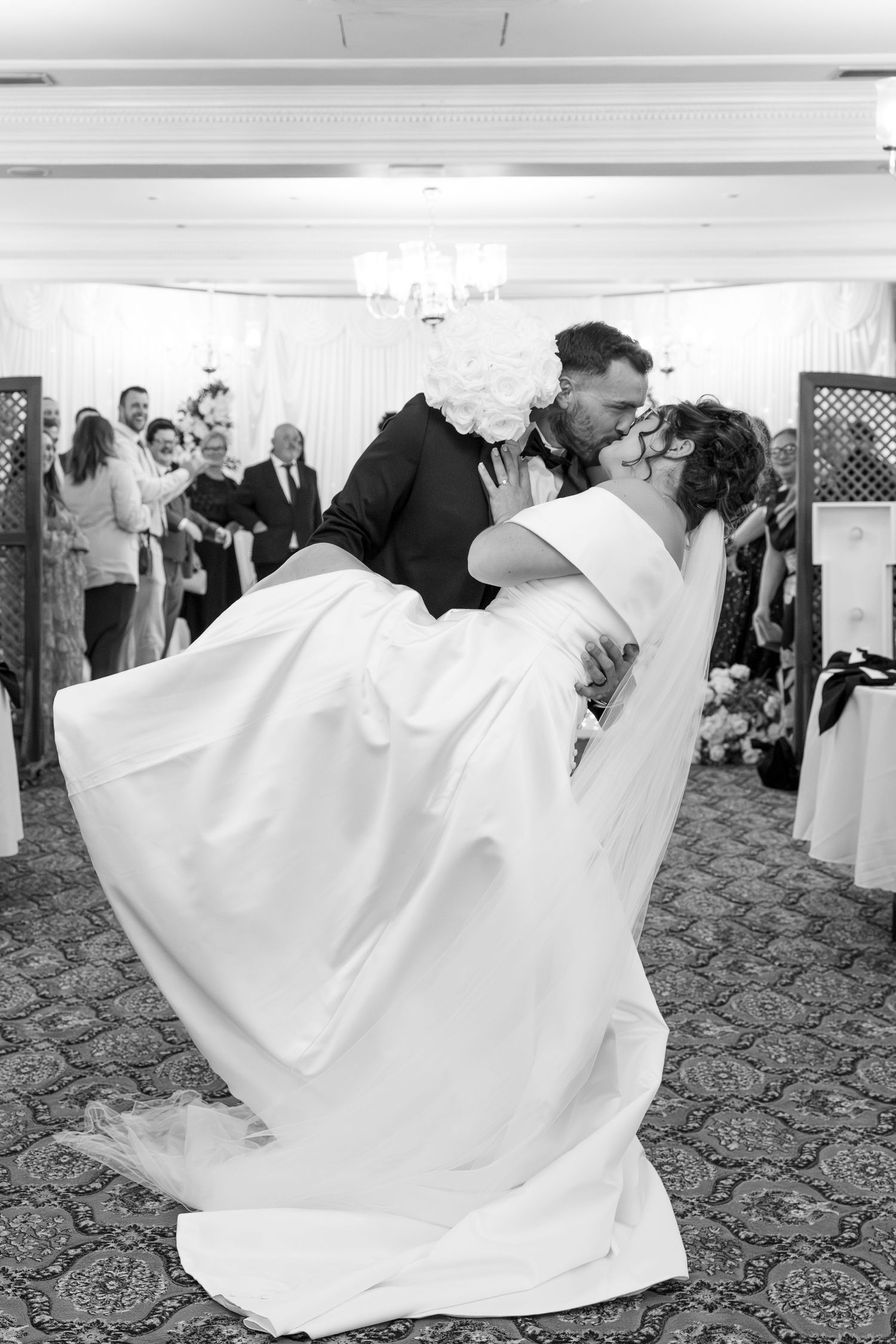 Black and white photo of groom lifting bride during first dance at wedding reception.