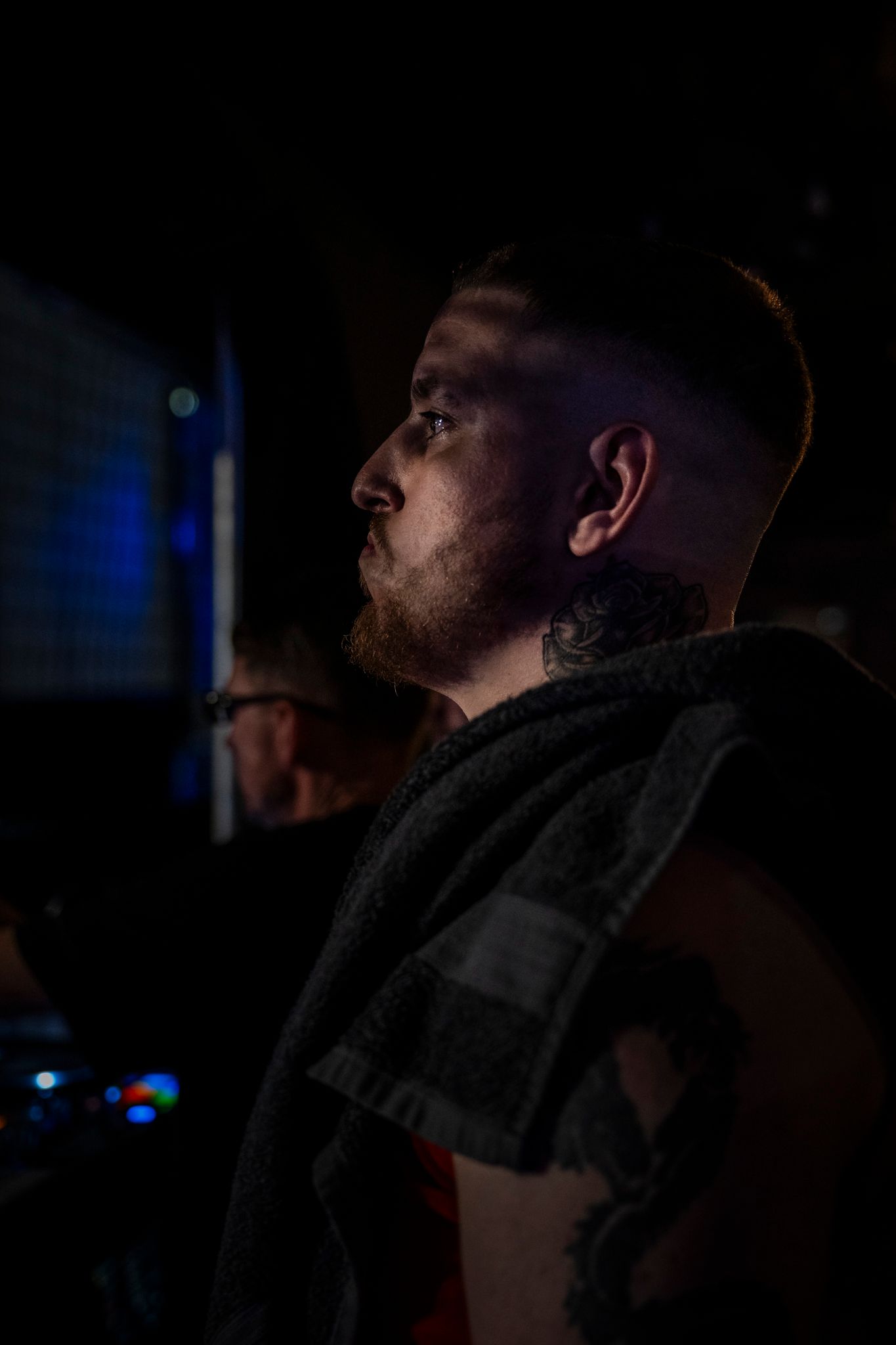 Side profile portrait of figure in dark clothing against dramatic low-light black background with blue lighting.