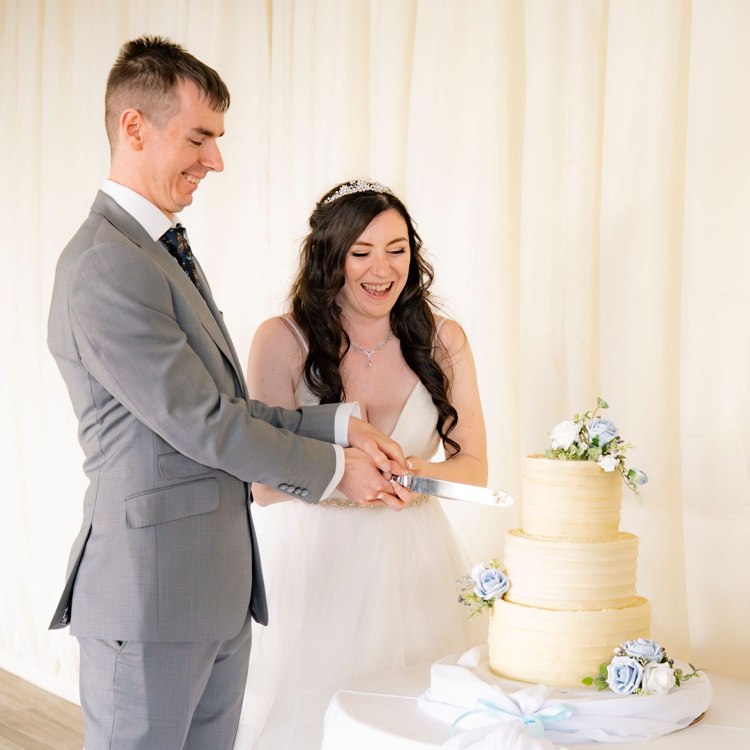 Wedding cake cutting ceremony with elegant yellow buttercream tiers decorated with blue flowers.
