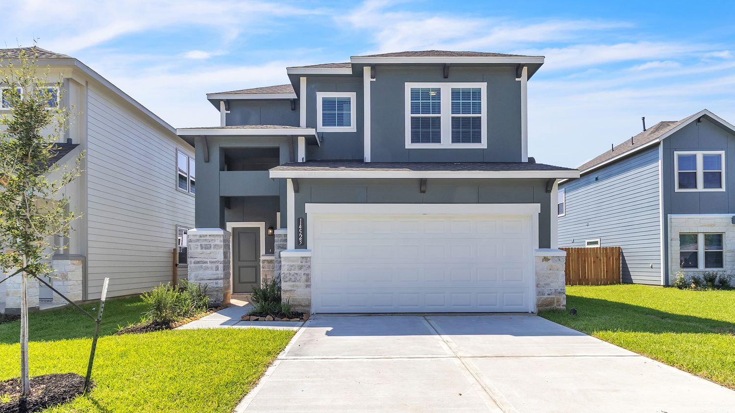 Contemporary gray and navy blue house with white trim and a well-manicured front lawn on a sunny day.