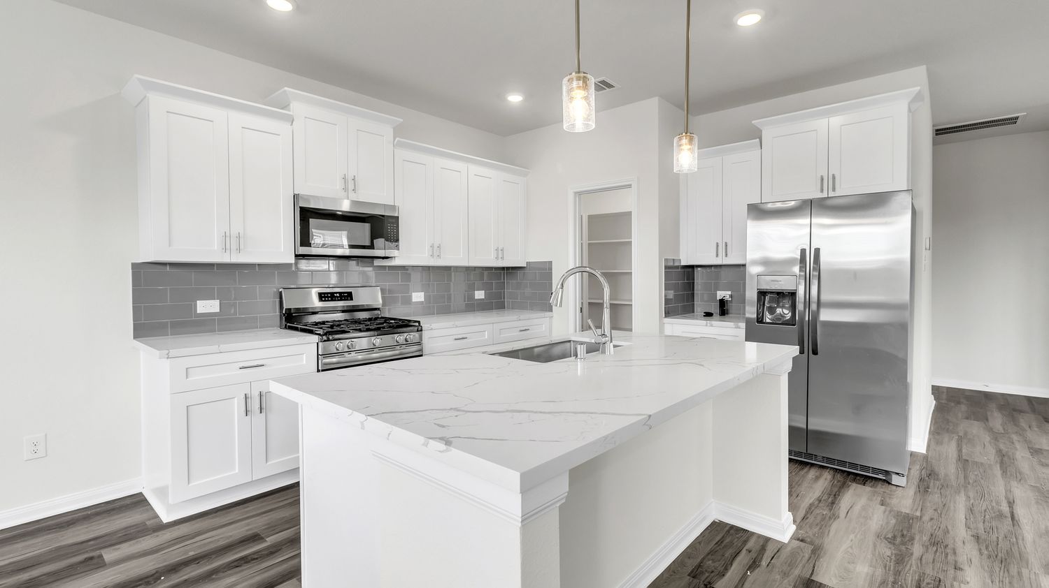 Modern white kitchen with gray quartz countertops, shaker cabinets, stainless appliances and luxury vinyl plank flooring.