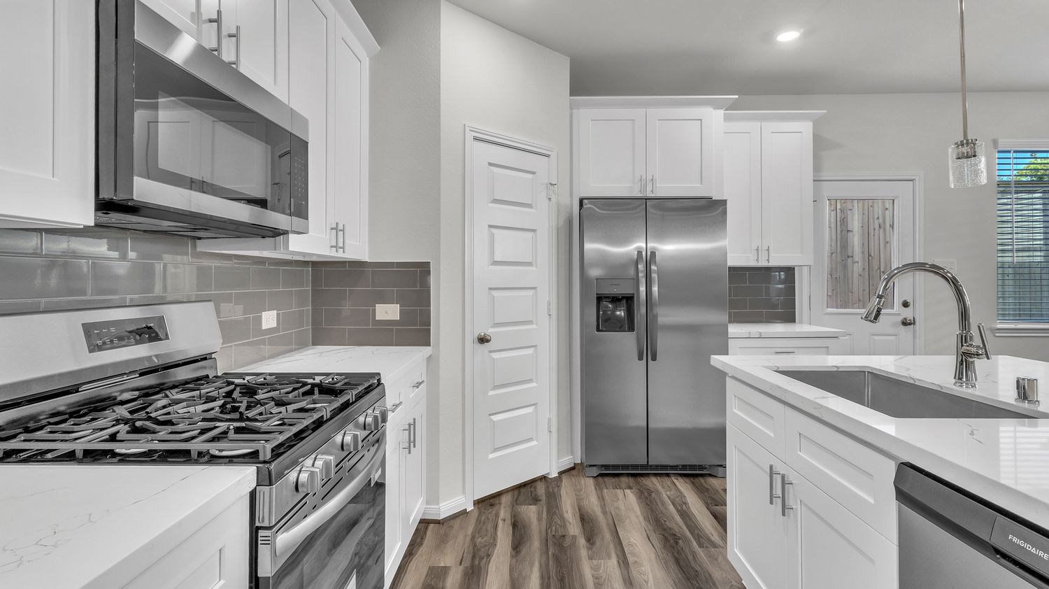 Modern white kitchen interior with stainless steel appliances, quartz countertops and recessed lighting.