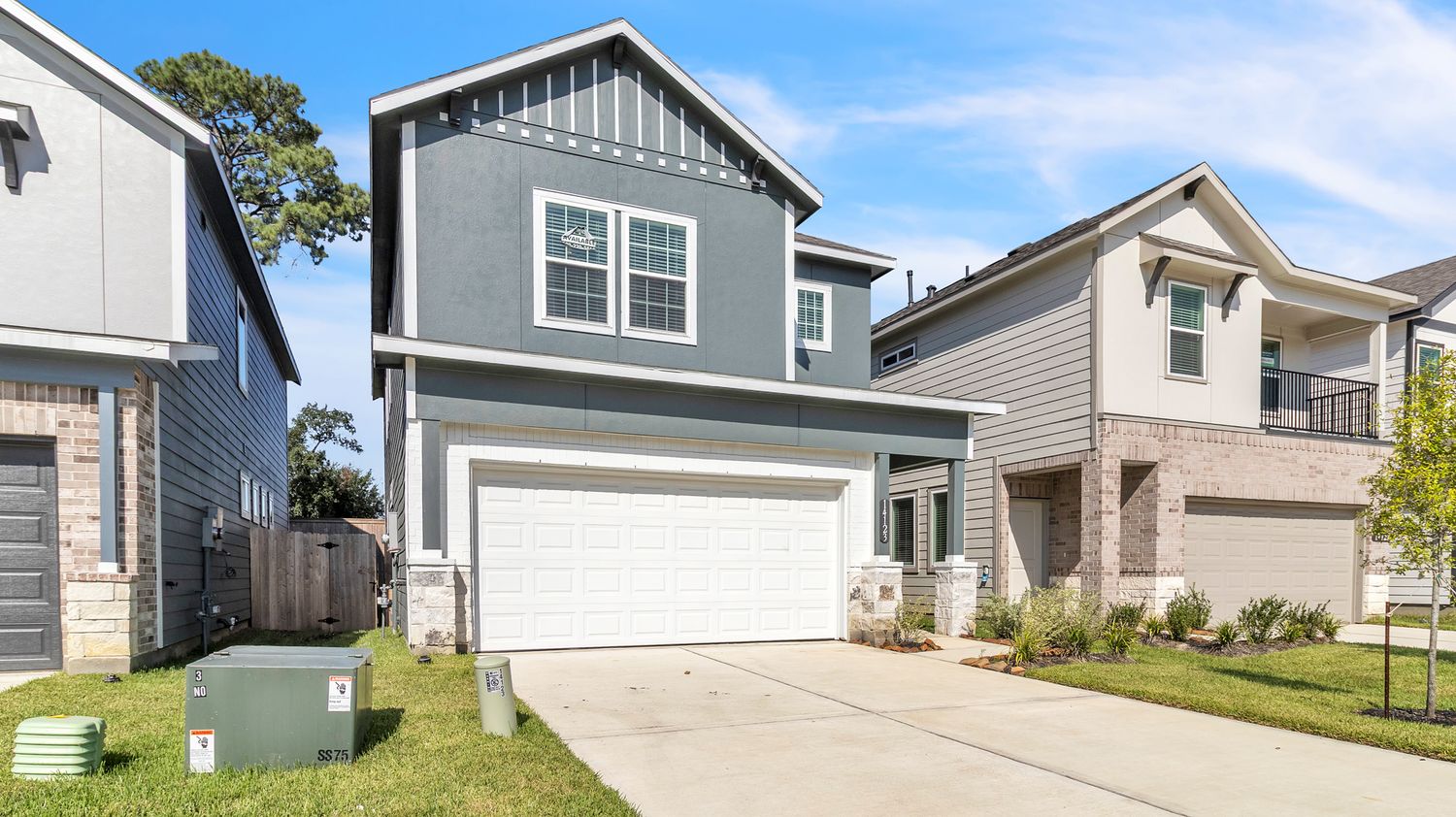 A panoramic view of modern suburban homes with gray siding and stone accents along a residential street.
