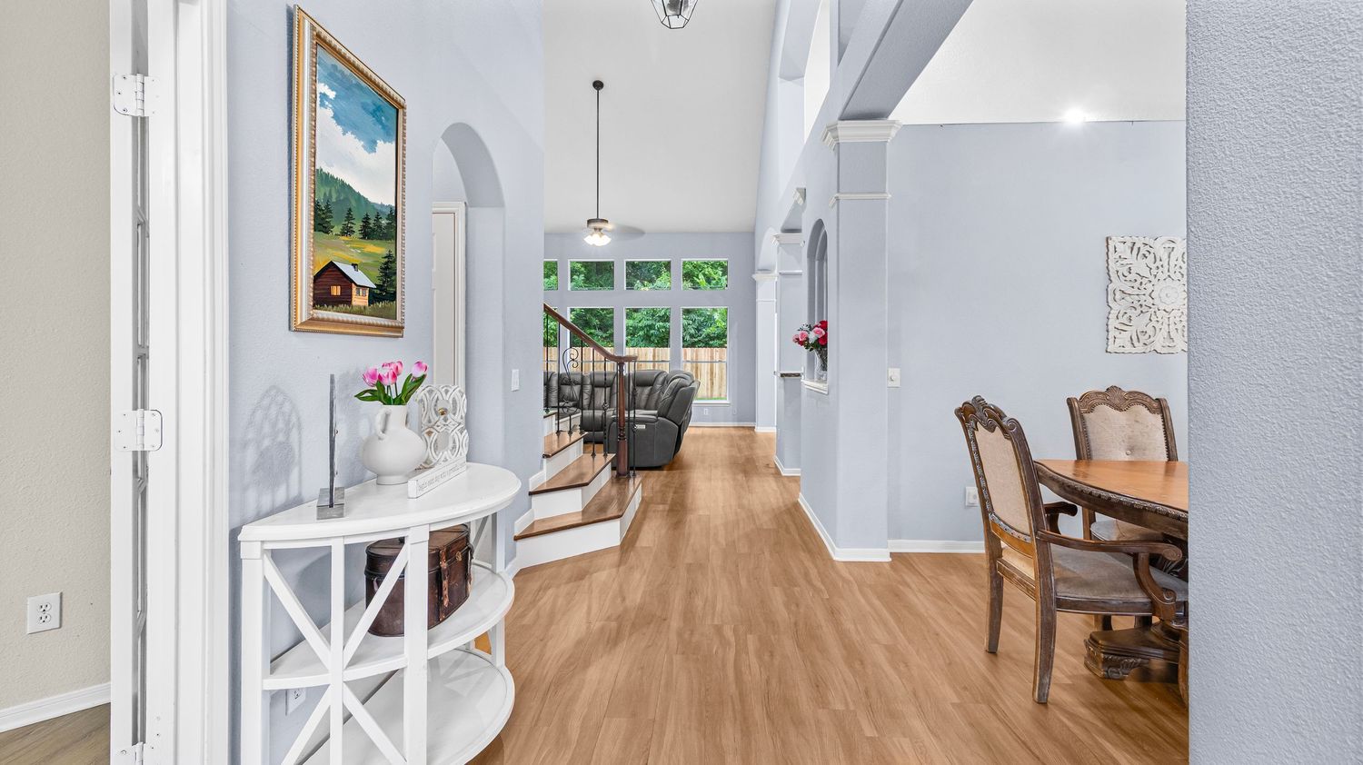 Bright hallway with hardwood floors, white walls, arched doorways, and a dining area with wooden chairs in a modern home.
