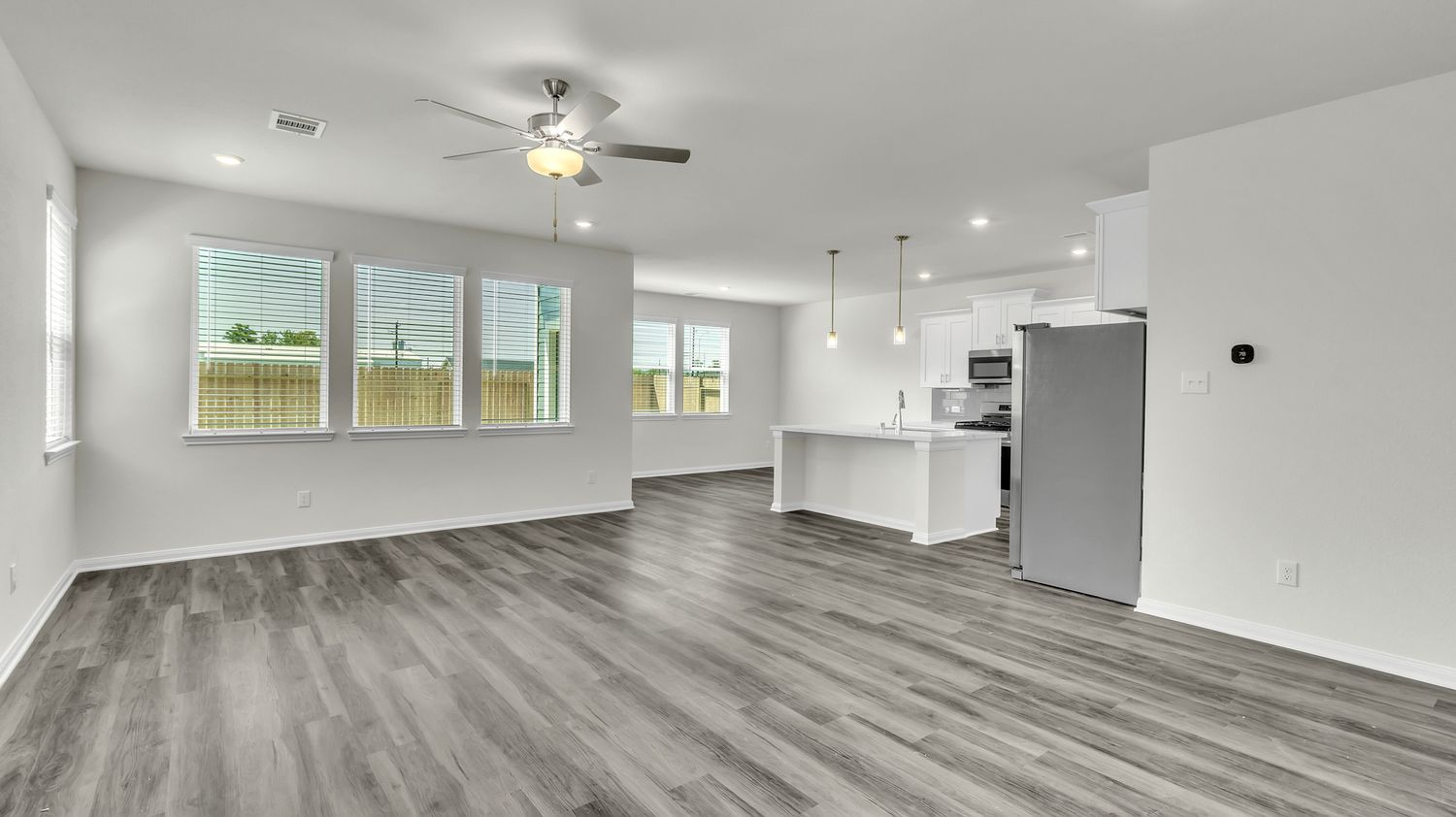 A panoramic view of an empty, modern room with gray hardwood floors, white walls, and ceiling fan fixtures.