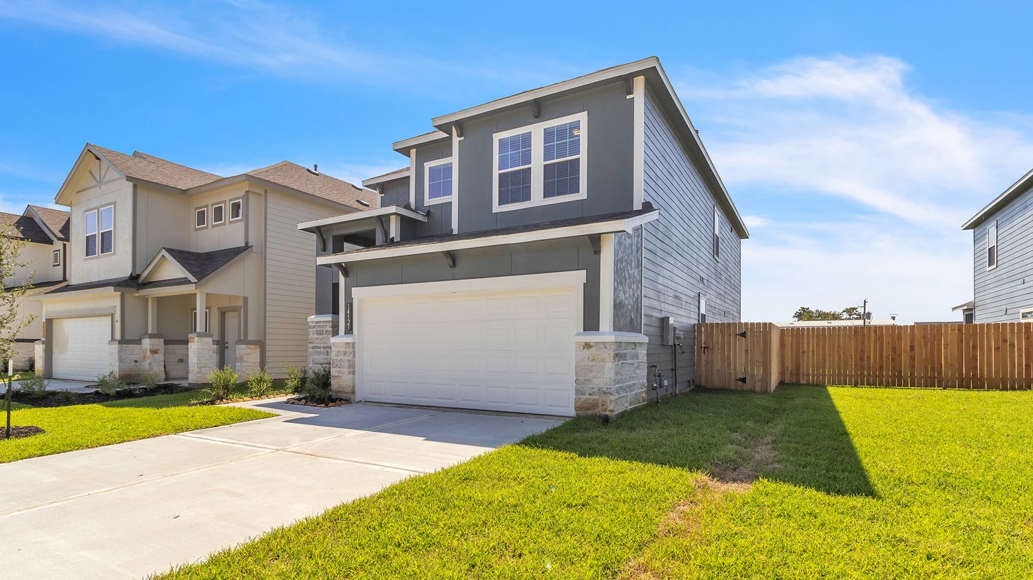 A panoramic view of modern suburban houses with landscaped lawns and driveways under a bright blue sky.