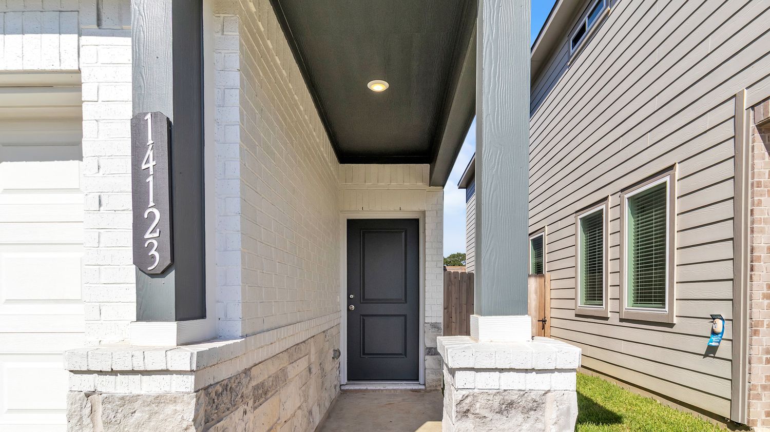 Row of exterior doorways and light fixtures on white siding of residential properties on cloudy day.