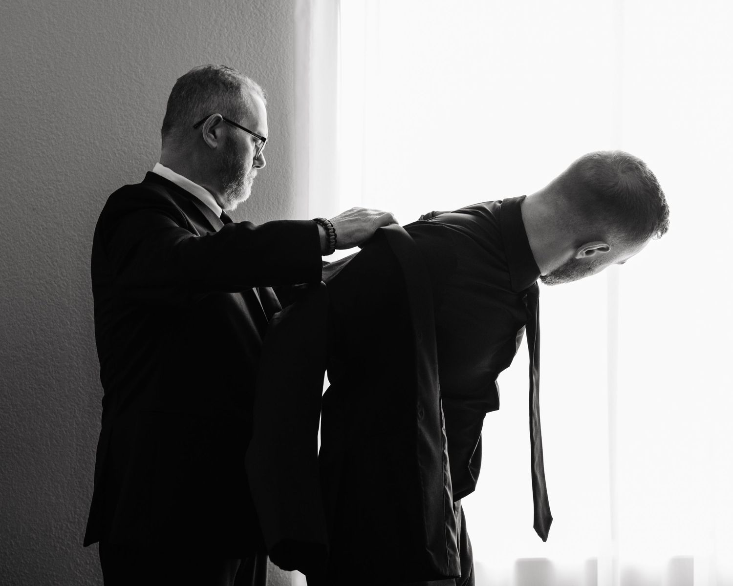 Father helping groom put coat on