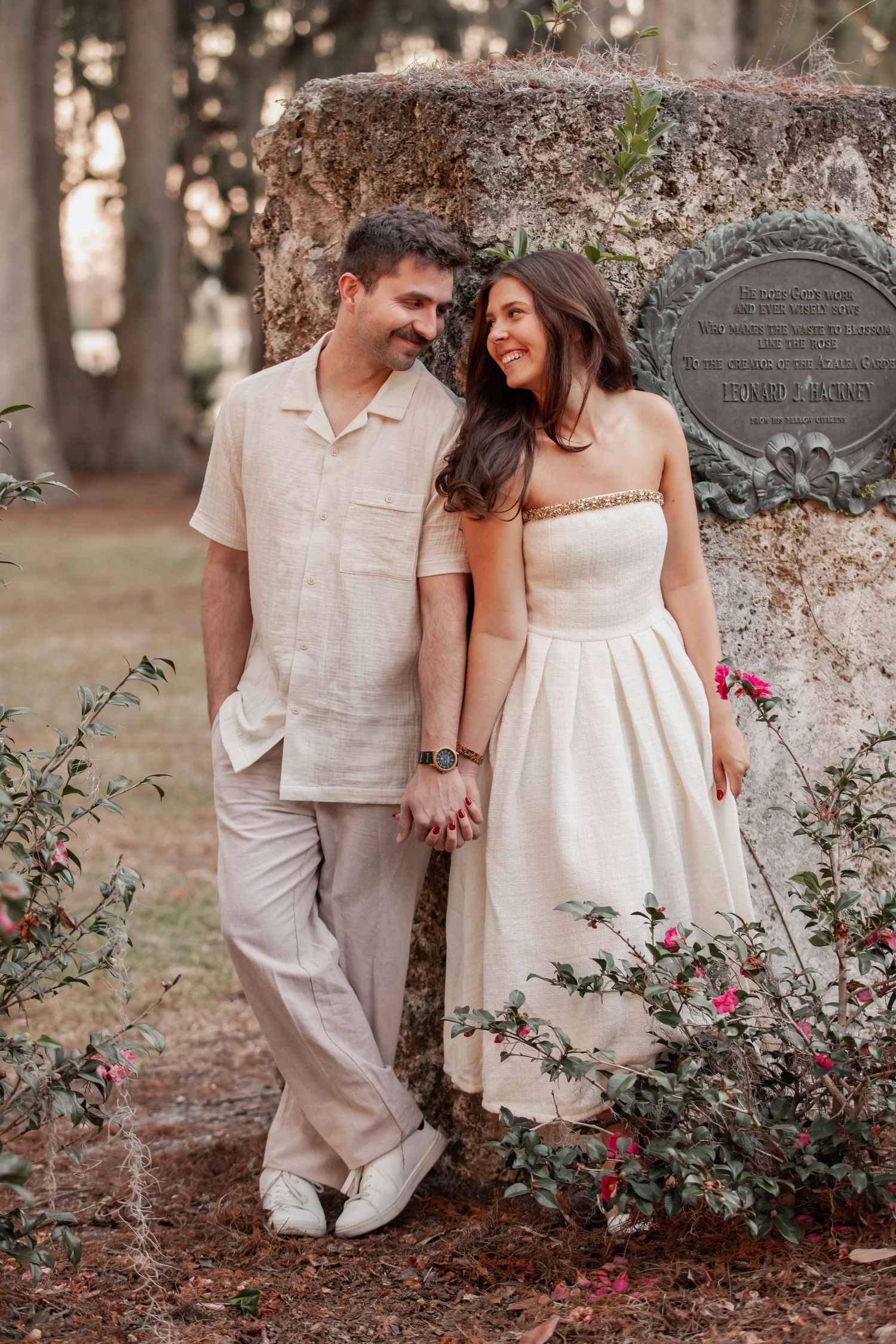 Engaged couple holding hands beneath cypress trees at Kraft Azalea Garden
