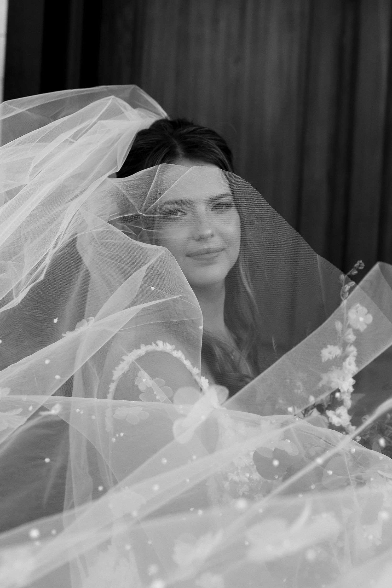 Black and white portrait of a bride smiling softly beneath a flowing tulle veil adorned with pearls.