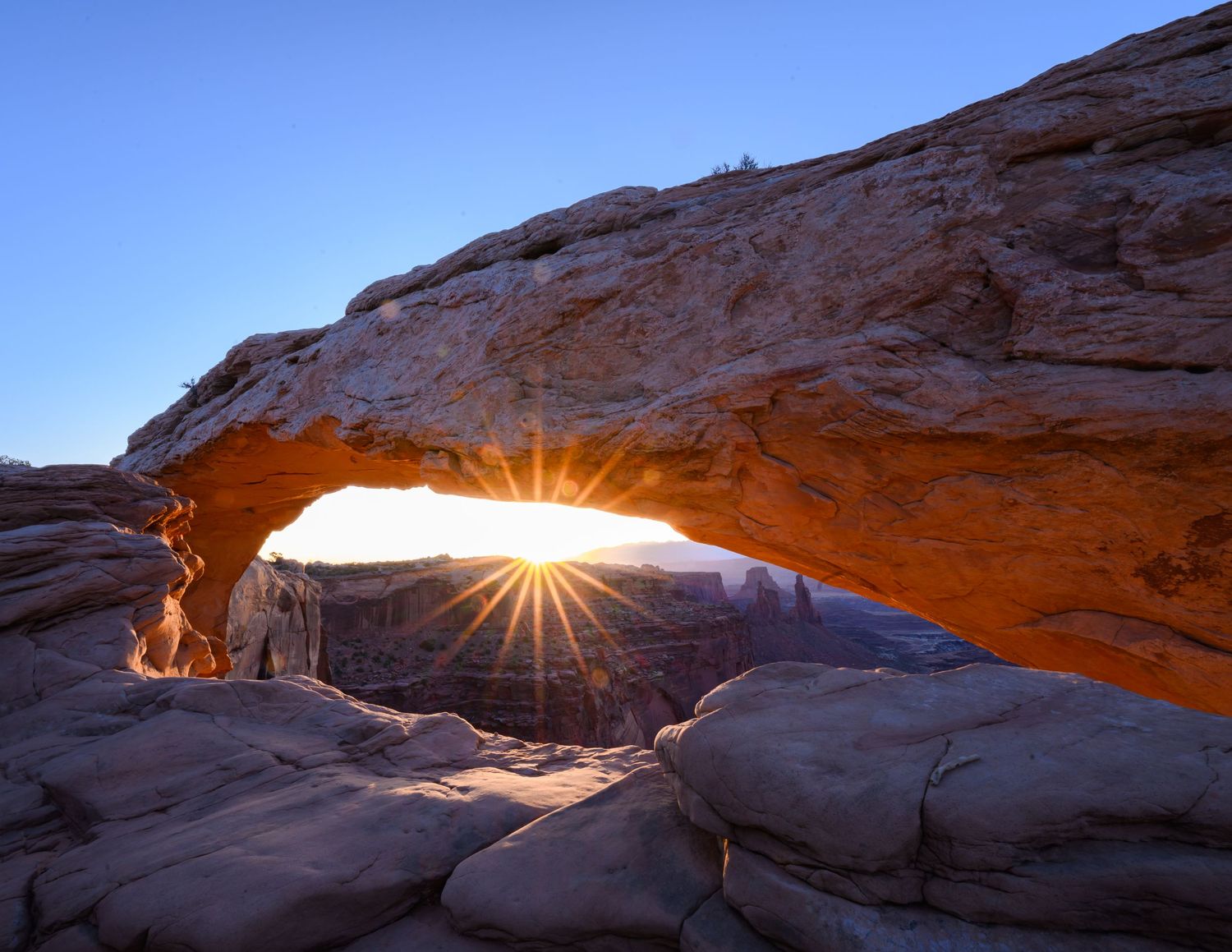 First light bursts through Mesa Arch in Canyonlands National Park, casting a warm glow across the desert landscape.