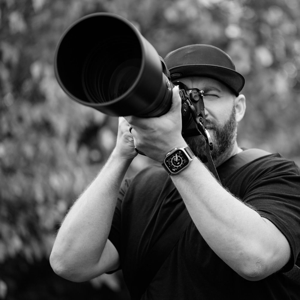 Black‑and‑white shot of Shawn Thomas aiming a super‑telephoto lens, ready to capture wildlife through the glass.