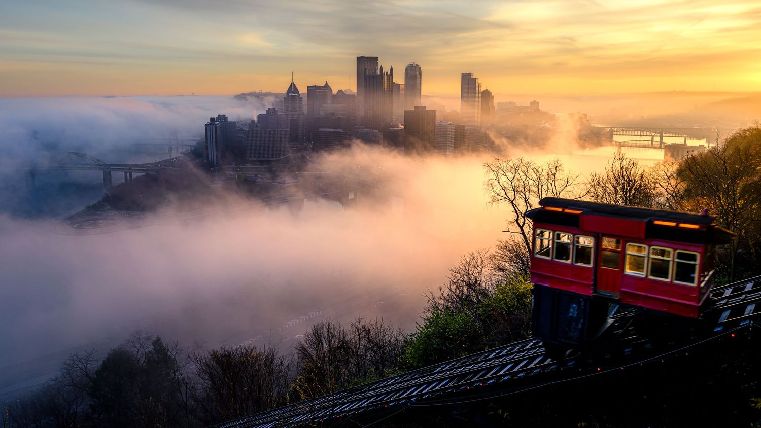 Pittsburgh skyline rises through morning fog as the Duquesne Incline climbs the hillside at sunrise.