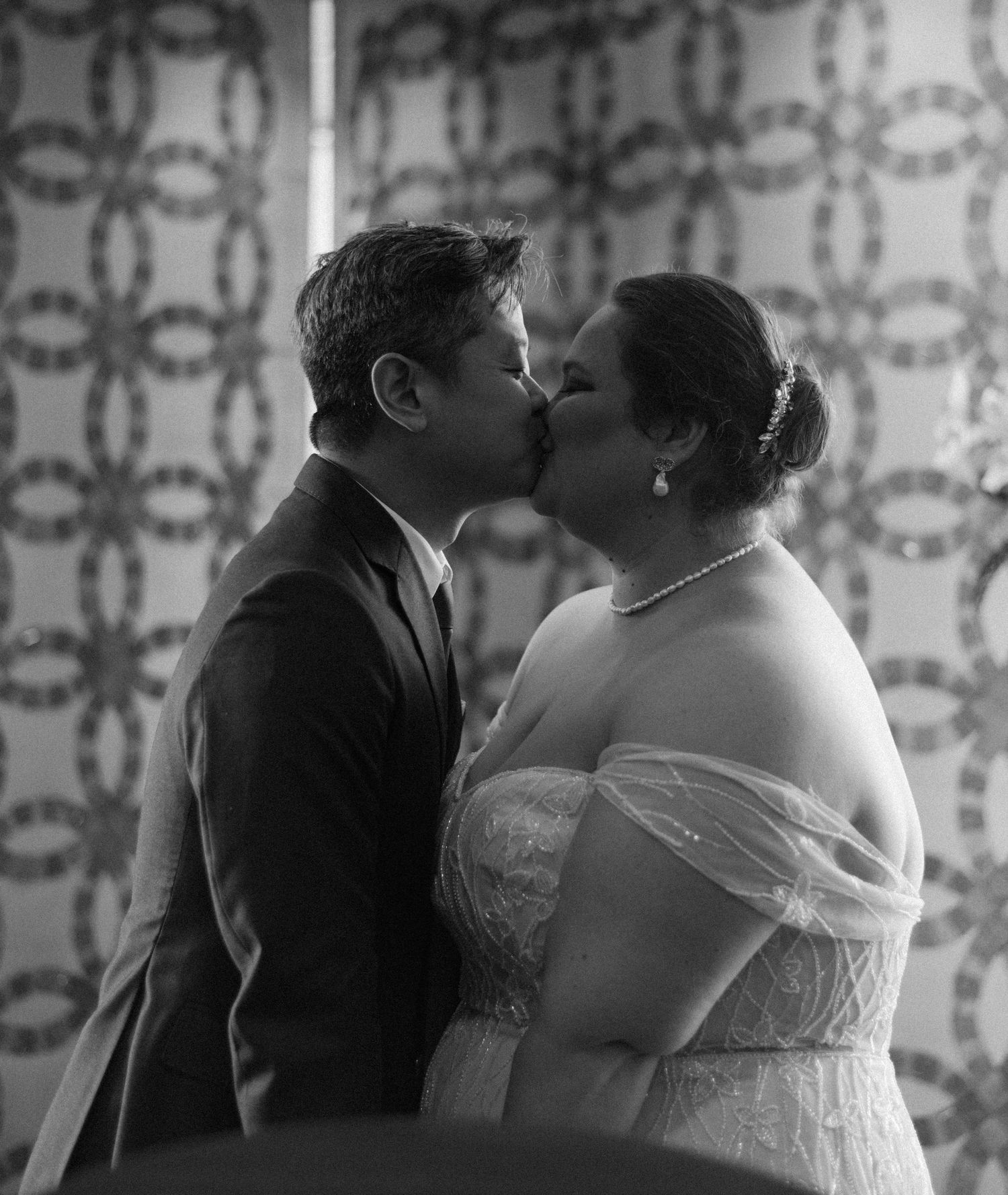 Intimate black and white portrait against vintage wallpaper background.