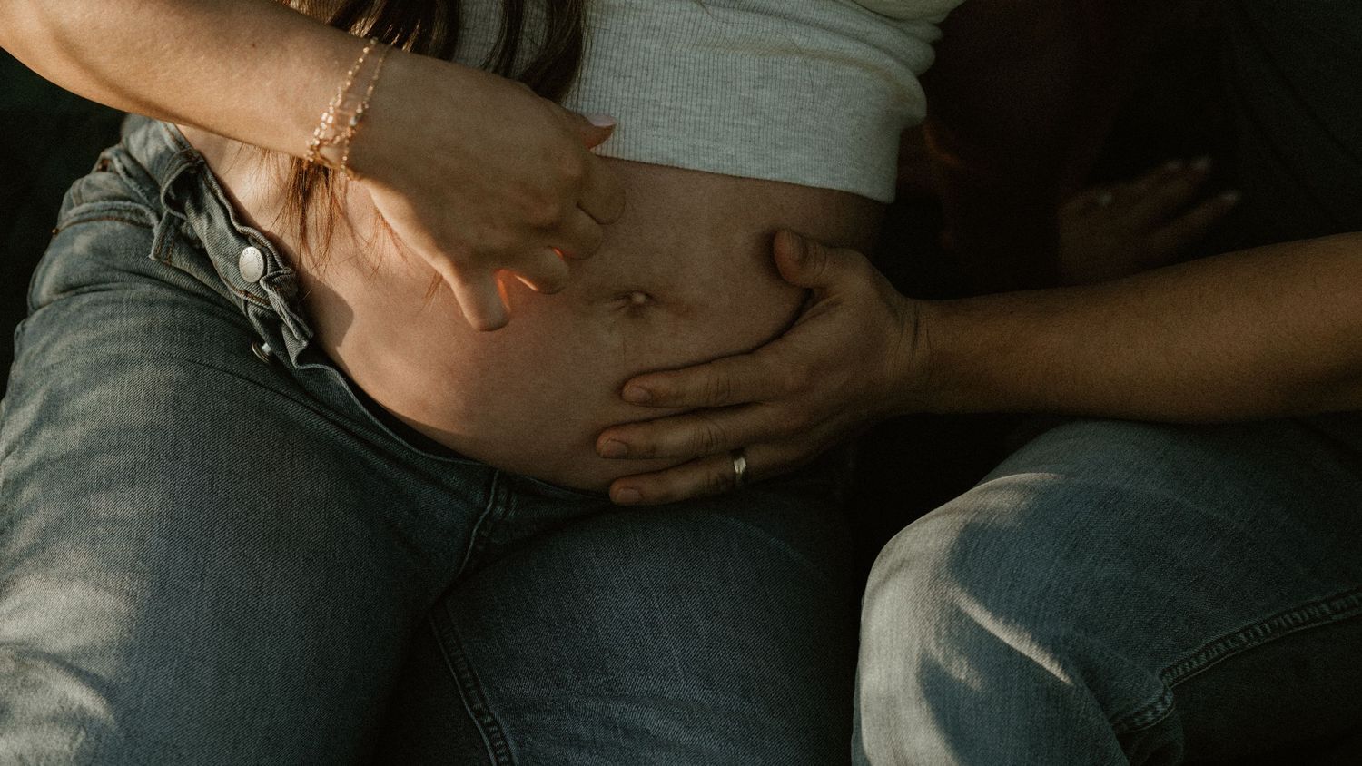 Intimate maternity photo showing hands gently cradling a pregnant belly in soft lighting.