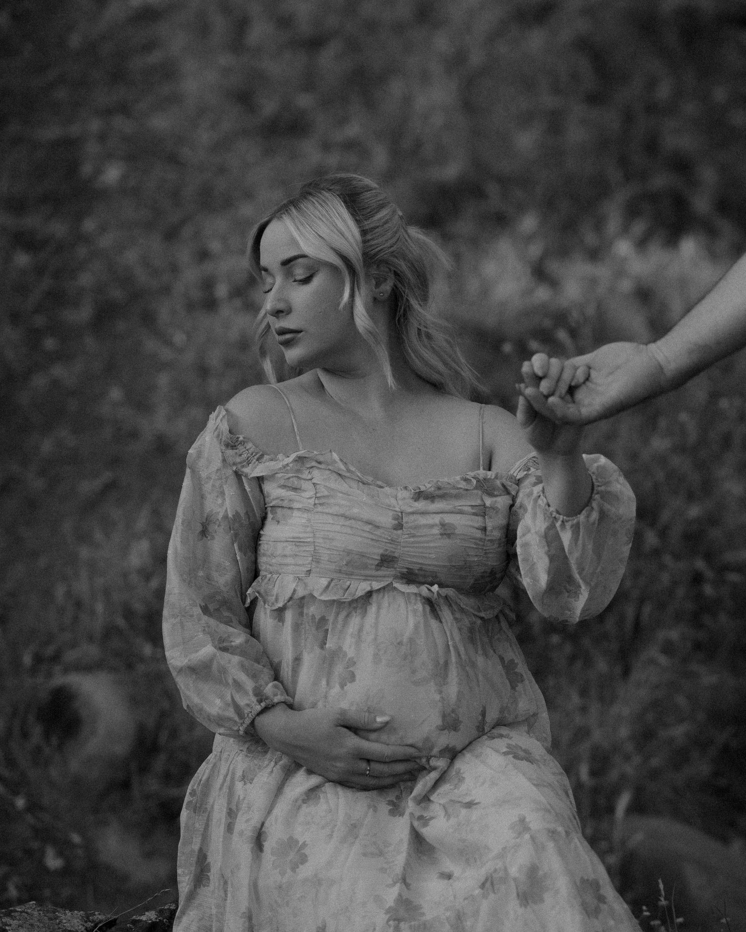 Romantic black and white maternity portrait in a flowing dress outdoors.