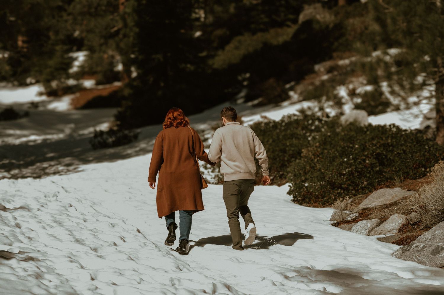 A couple walking hand in hand along a snowy winter trail.
