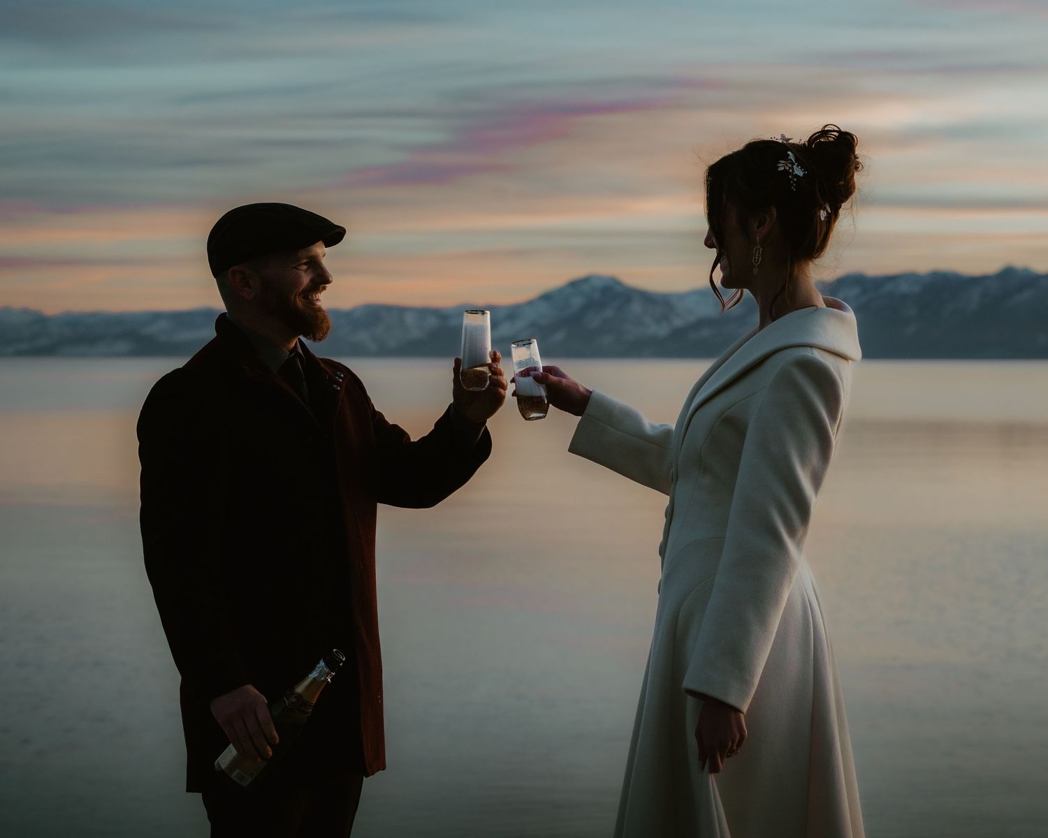 Two silhouetted figures share a romantic moment against a serene waterfront sunset backdrop.