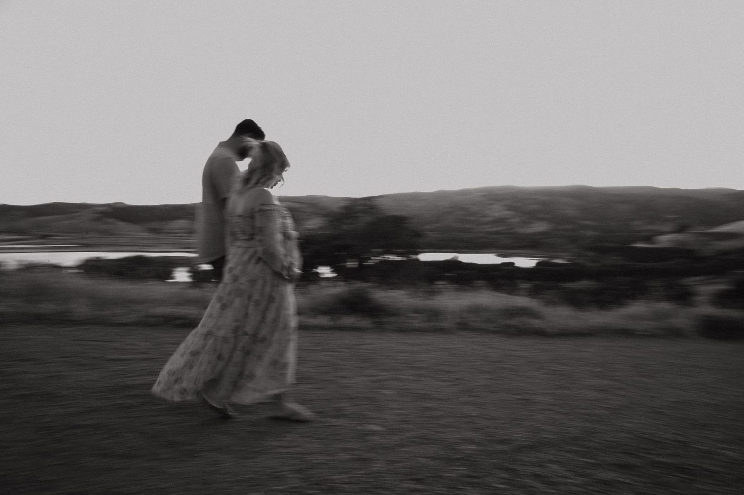 Ethereal black and white photo of figure in flowing dress against rural landscape.