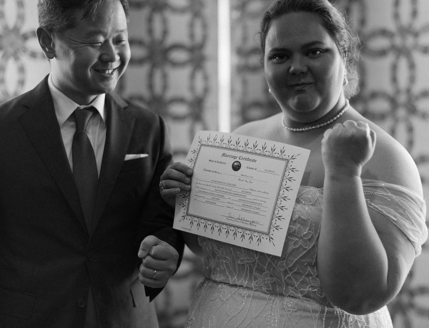A joyful couple displays their marriage certificate in a candid black and white photo.