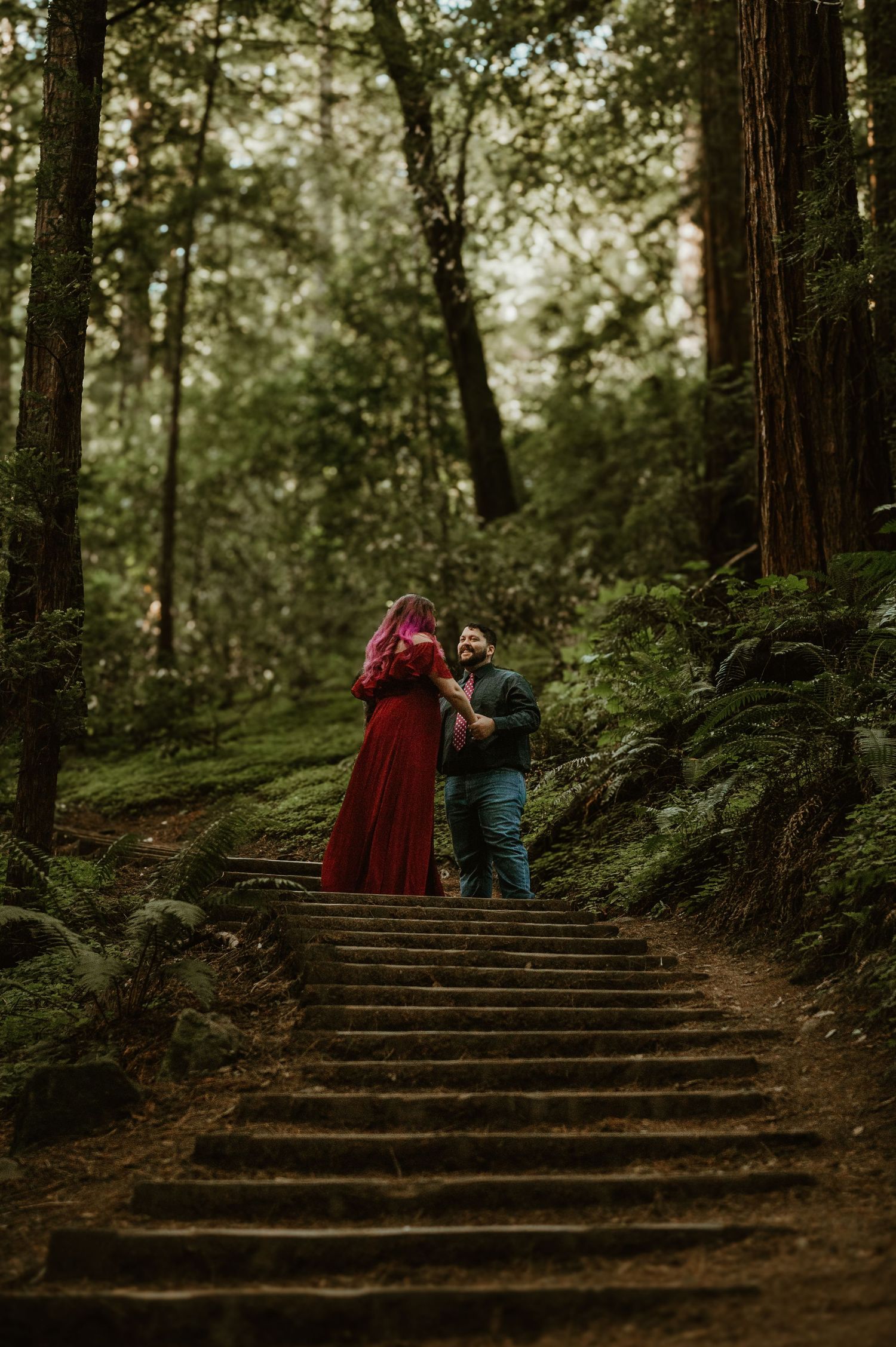 Two figures ascending wooden steps through a misty redwood forest.