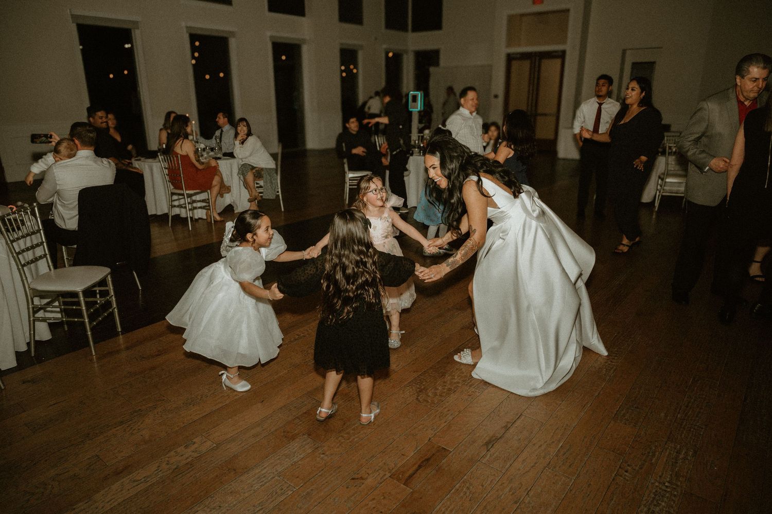 Wedding guests and children dancing together on a wooden dance floor during reception celebrations.