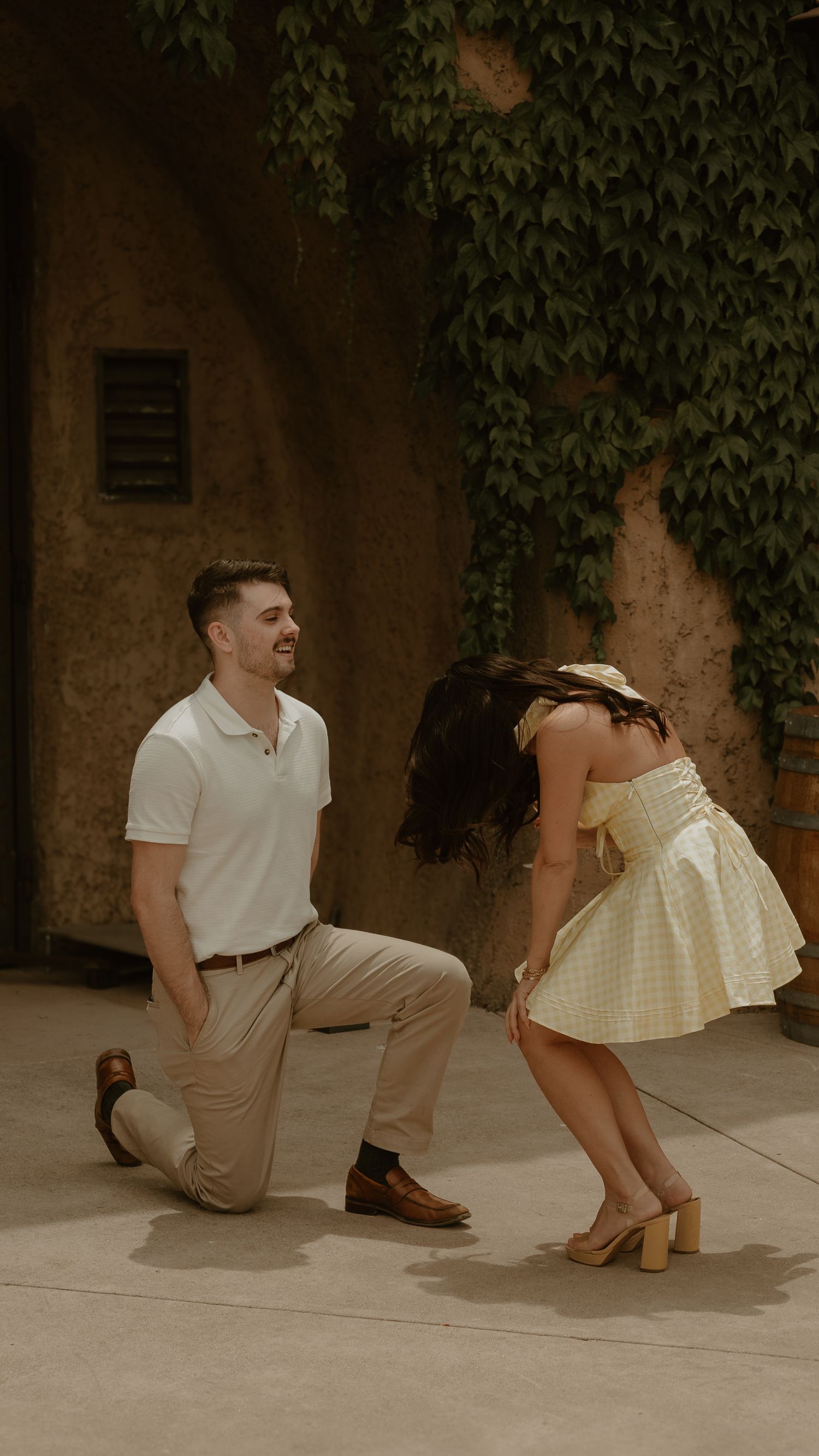 A couple poses for stylish photos against an ivy-covered wall in summer attire.
