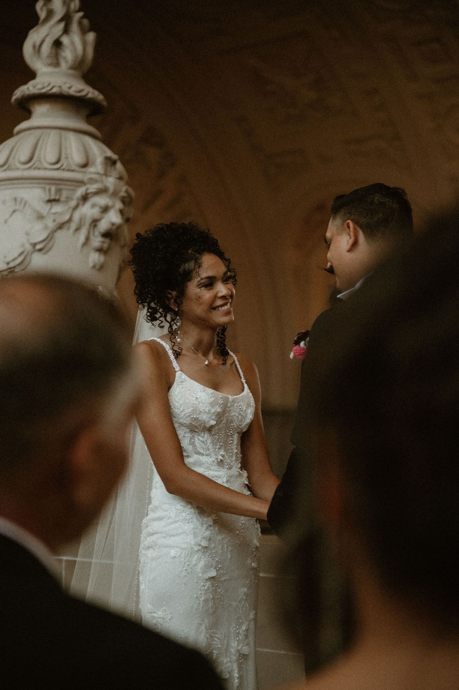 A couple exchanges vows during their wedding ceremony beneath an ornate white sculptural detail.