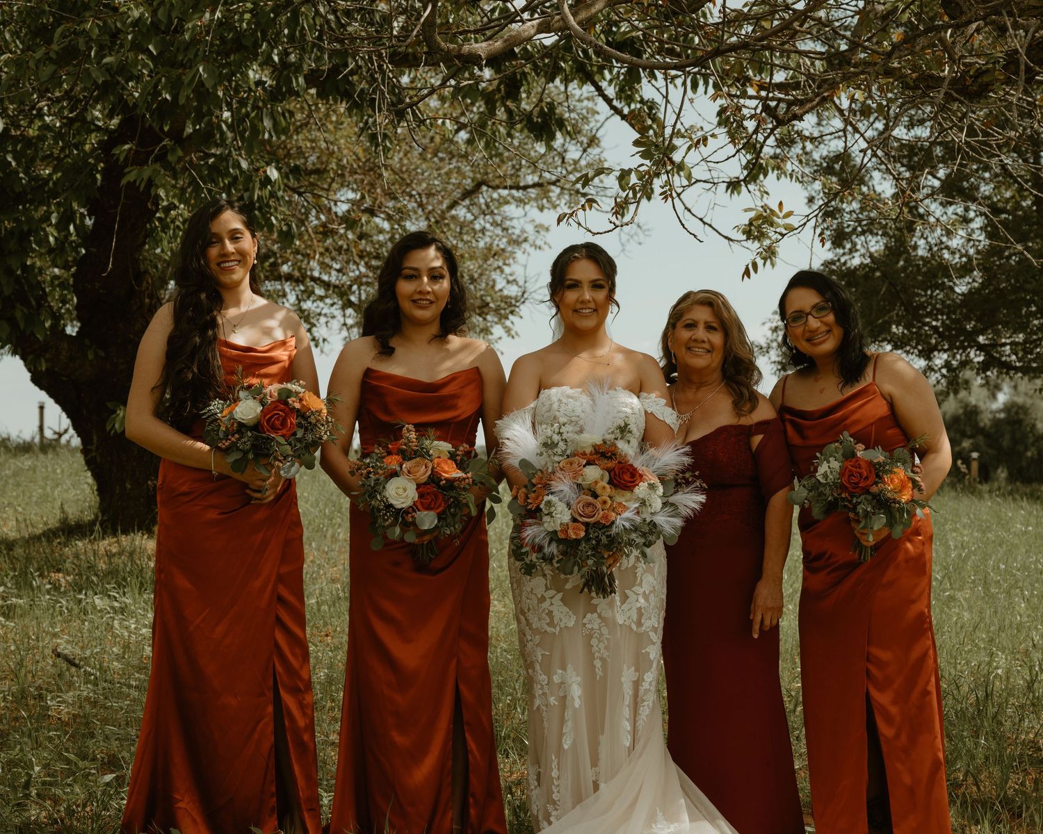 Bridal party in burgundy dresses holding bouquets poses outdoors.