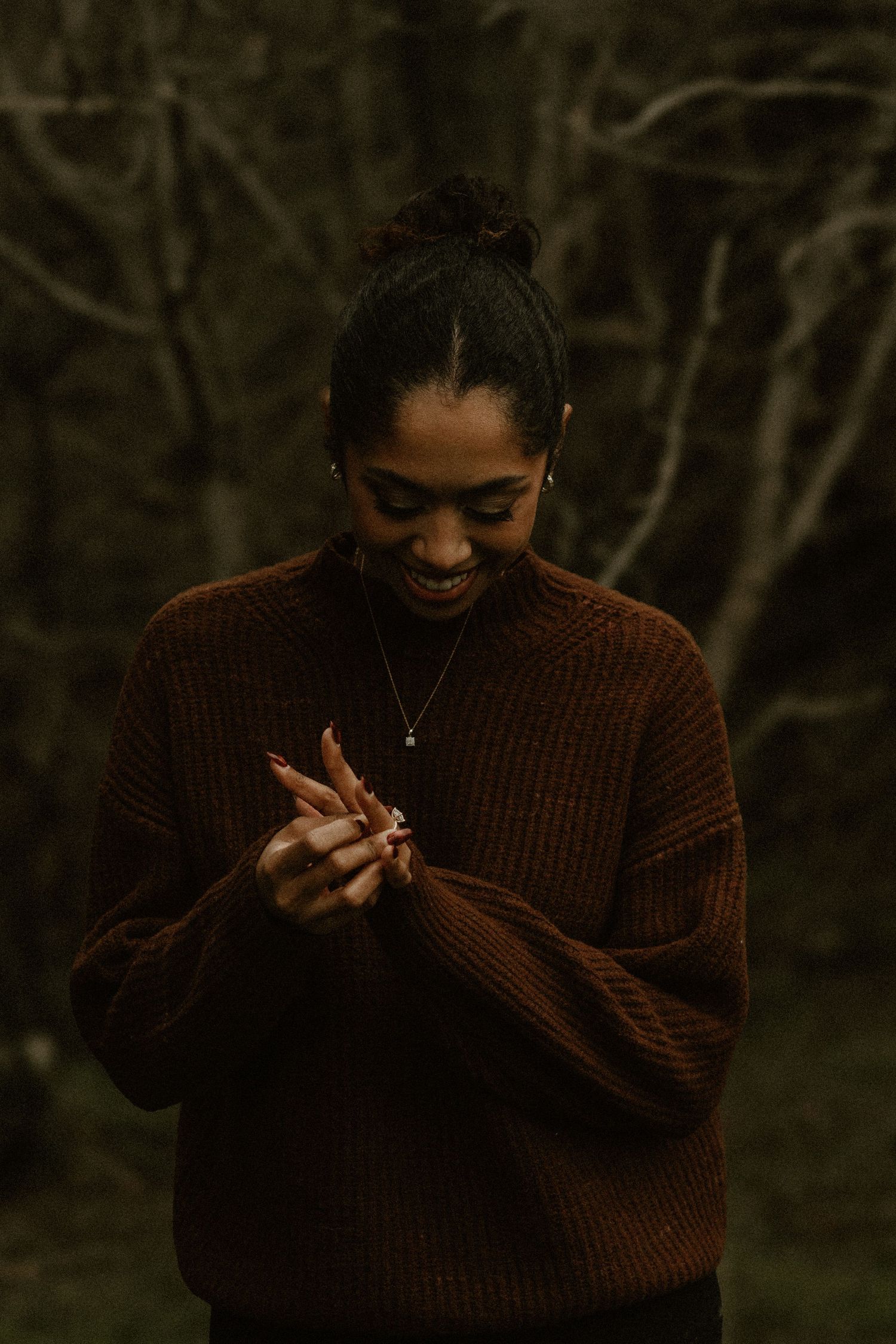 A person in a brown sweater photographed in a moody forest setting.