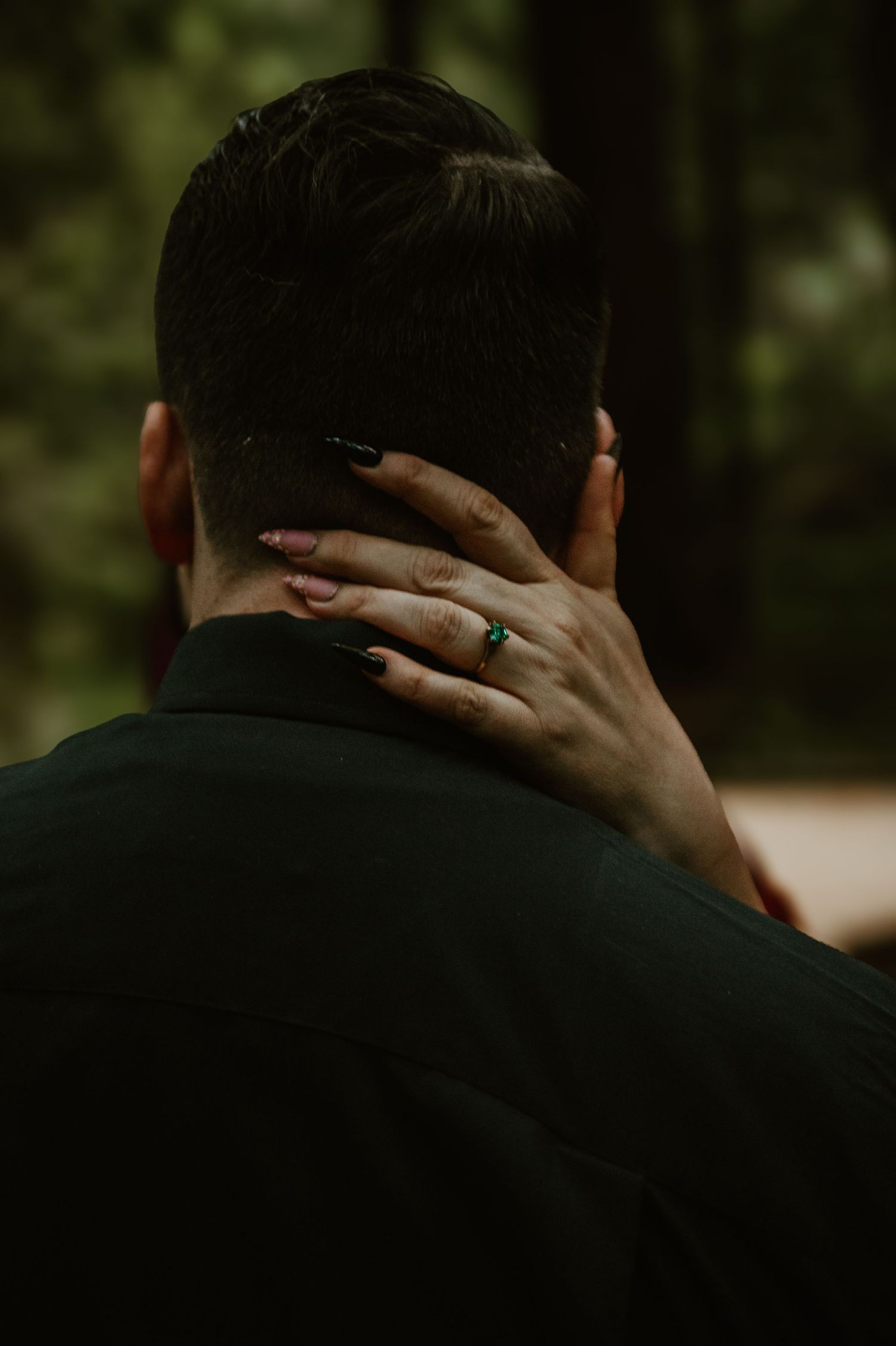 Close-up shot of hands tenderly touching the back of someone's neck against dark background.